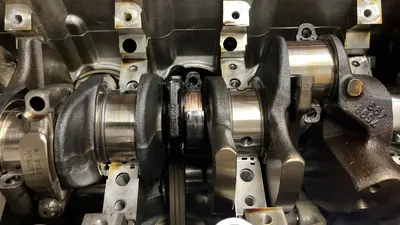 Crank with the block inverted: one journal dulled and coppered where the bearing spun; neighbors still polished. The failure that forced the rebuild.