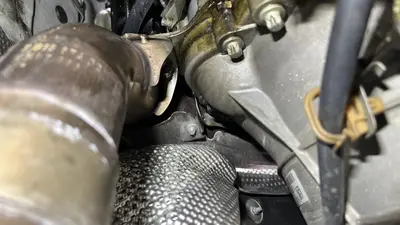 Under the heat shield: exhaust pipe and transmission bell housing — oil pooled at the low point of the bell housing.
