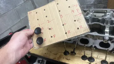 Cardboard valve/bucket map for one bank (cylinders 1–4, Ex+/Int, L/R, front marked). Head and carboned valves on the bench.
