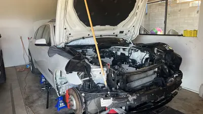 Engine out: empty bay, front end stripped, car on stands with the hood propped open.